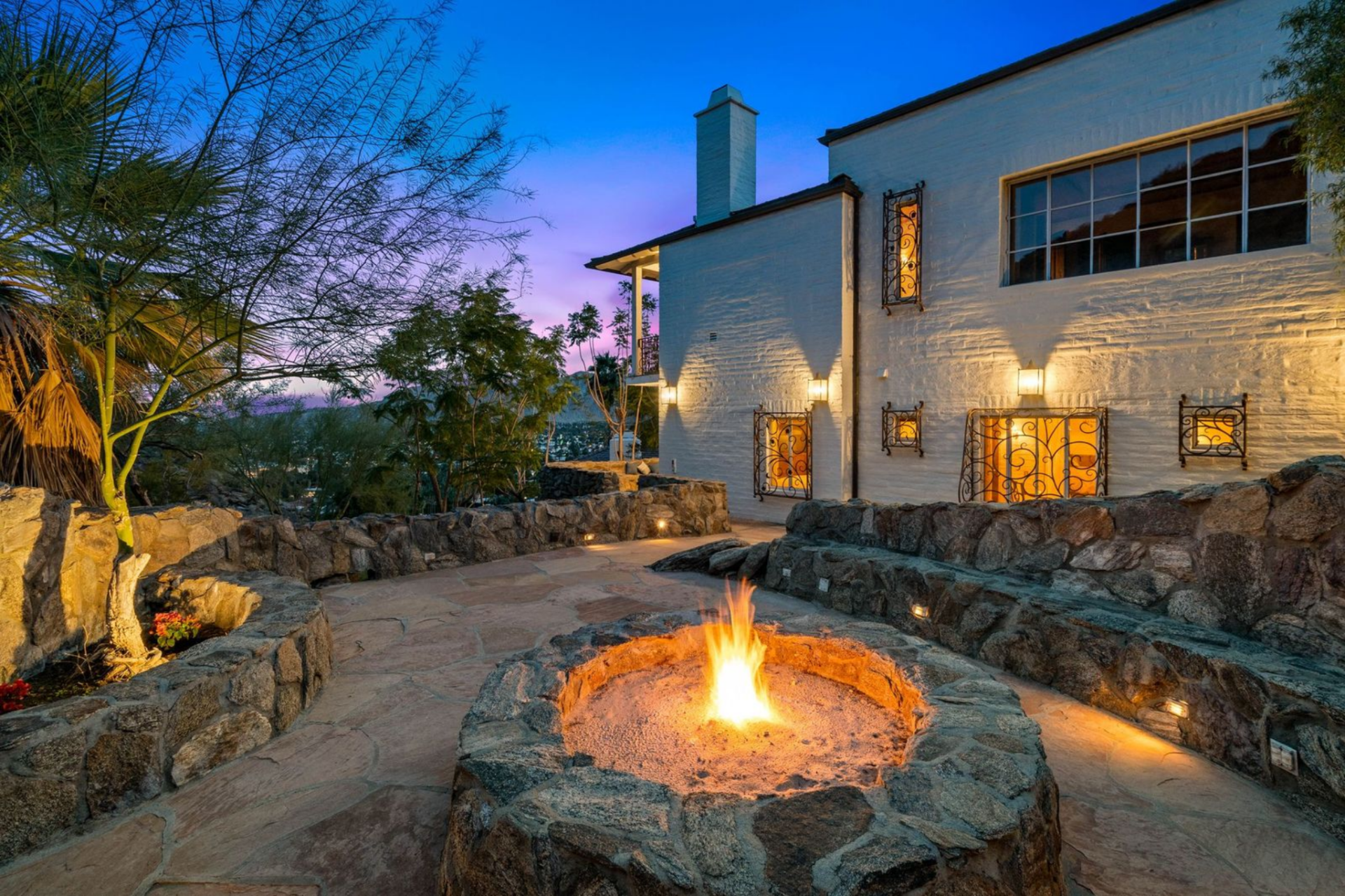 A circular firepit is built into another patio, surrounded by curved stone seating and integrated lighting.