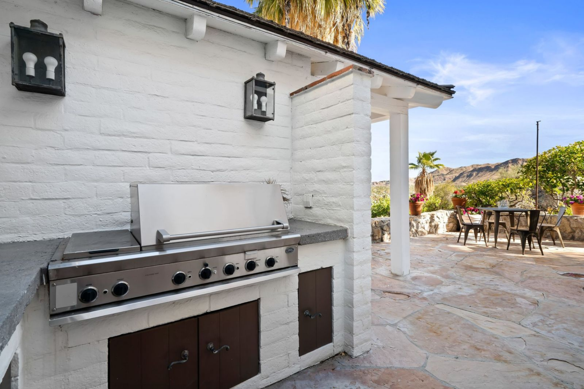 The outdoor kitchen is built into a white stucco wall just off a covered patio, with a built-in grill and prep space. 