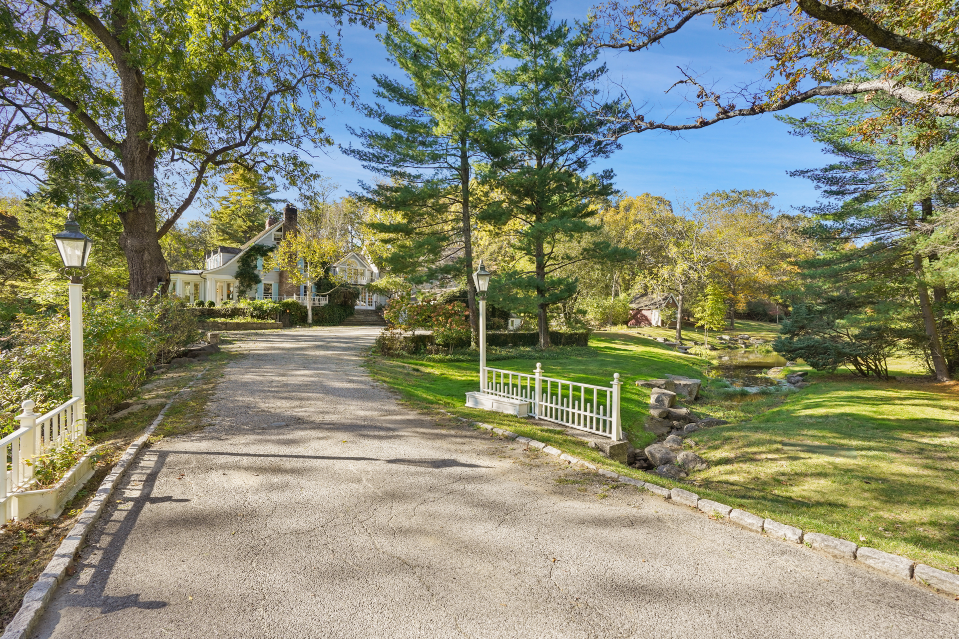 Long paved driveway framed by grass, streams, and tall trees that leads to the front of the house.