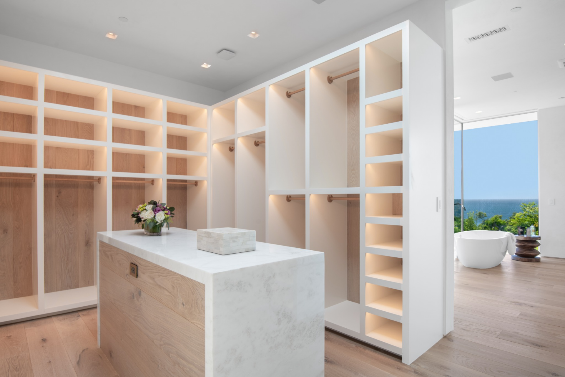 Lastly, the walk-in closet is laid out almost like a dressing room, with open shelving, hanging sections, and a center island finished in matching wood and stone.