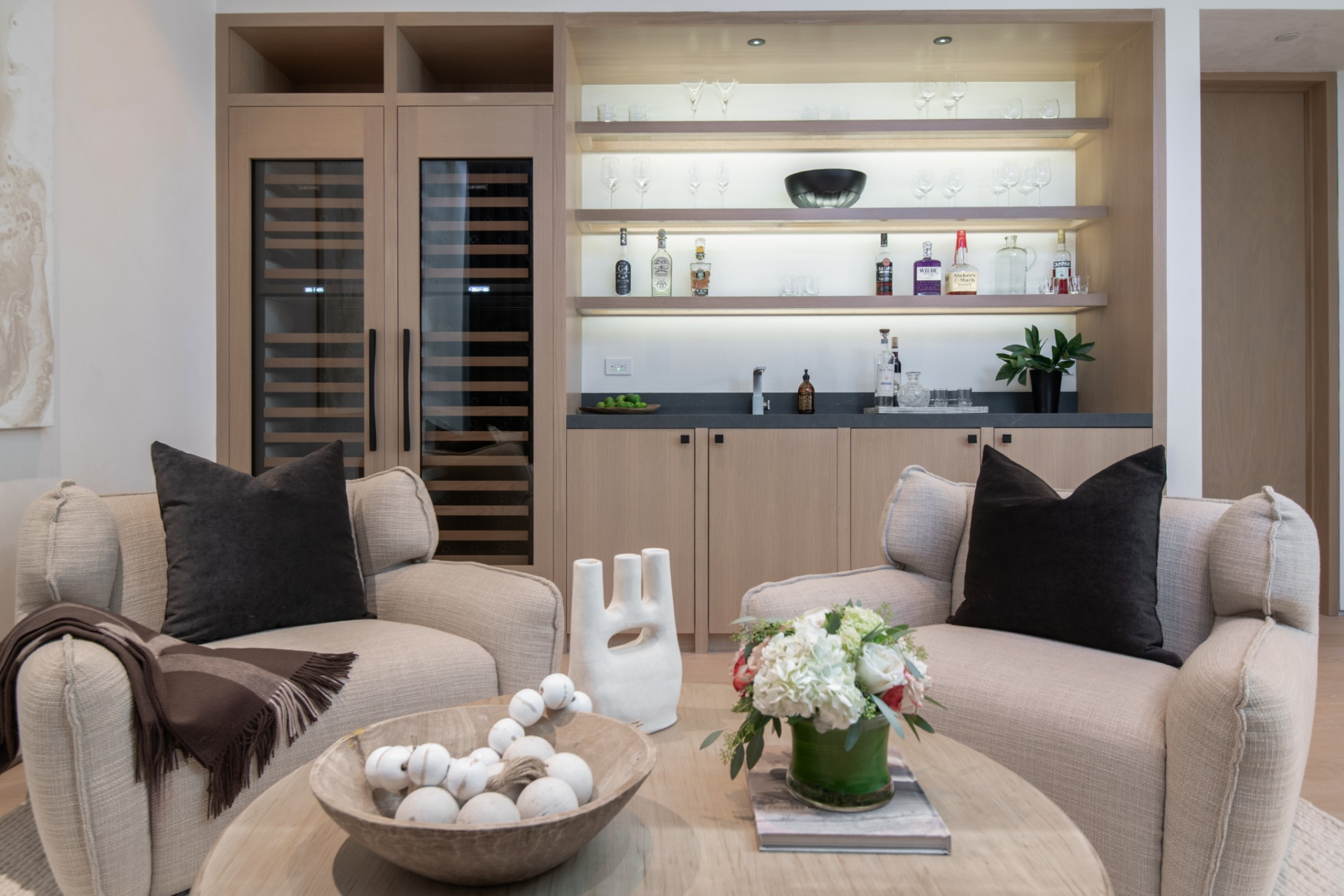 In the cellar, the bar lounge is set up as a compact sitting area with two built-in wine fridges, a wet bar, and open backlit shelving for glassware and bottles.