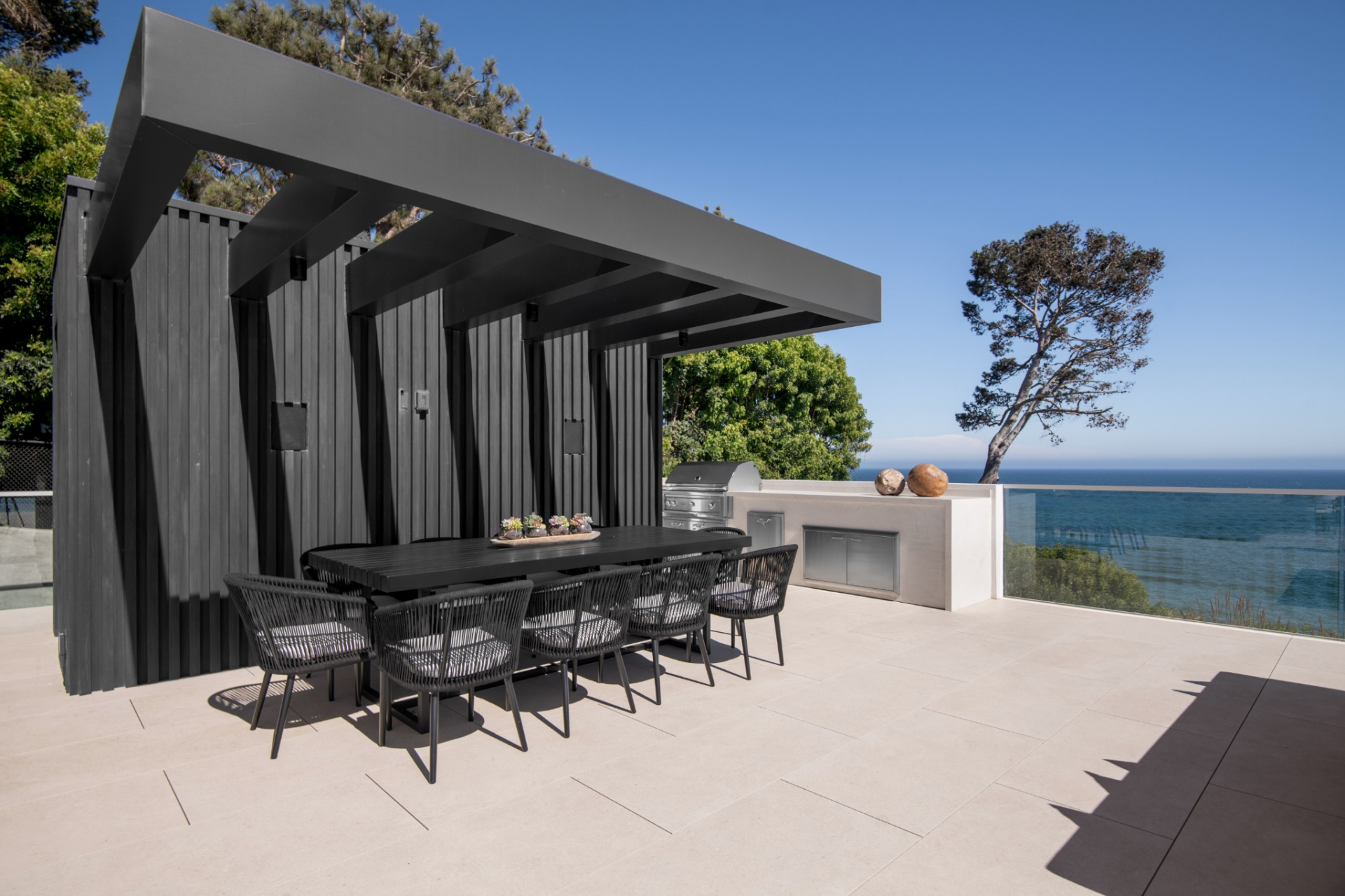 A long dining table is centered below it, while the open sides keep the ocean view and the surrounding landscape visible.