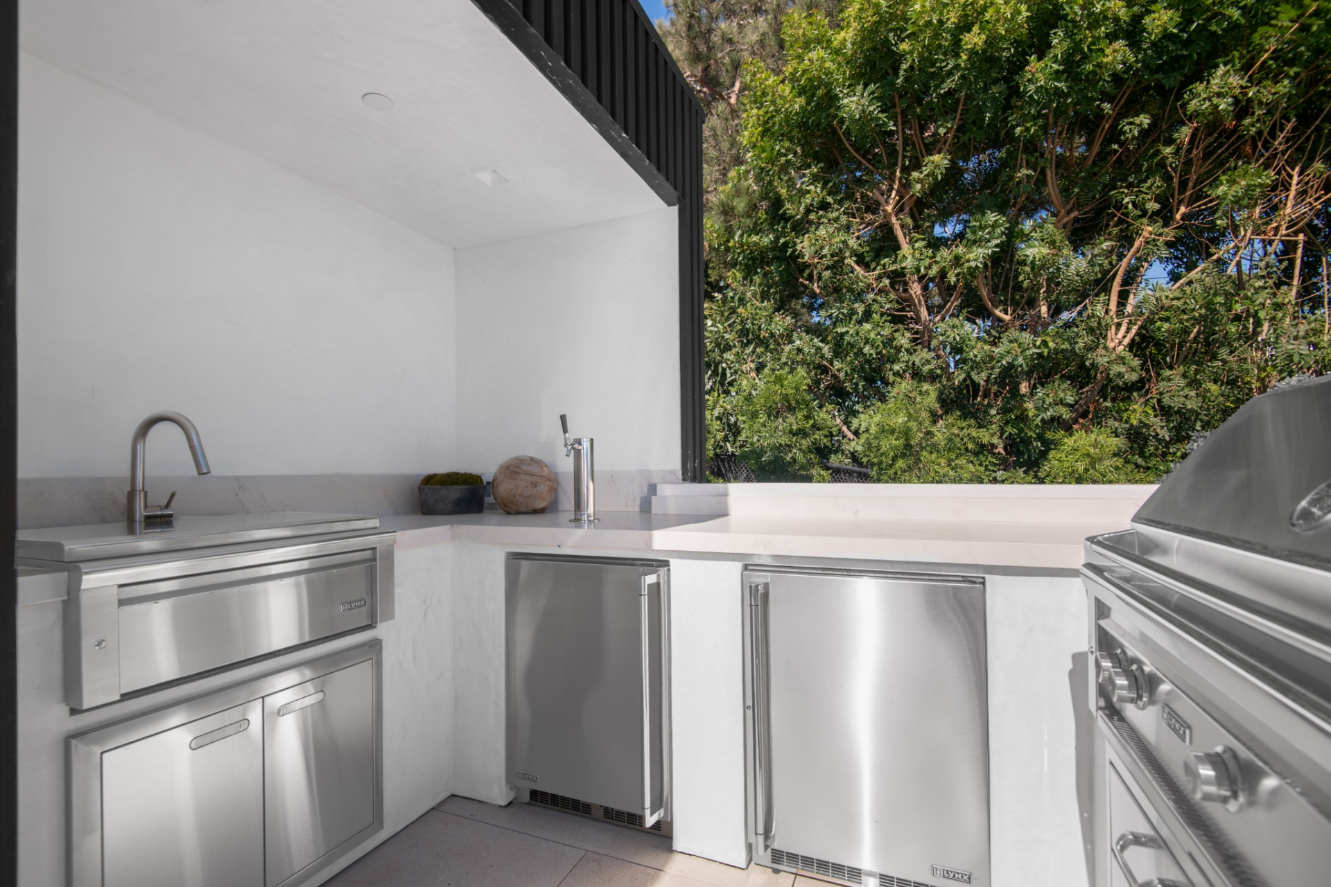 Around the corner is a barbecue station with stainless appliances, undercounter refrigeration, storage, a sink, and prep space.