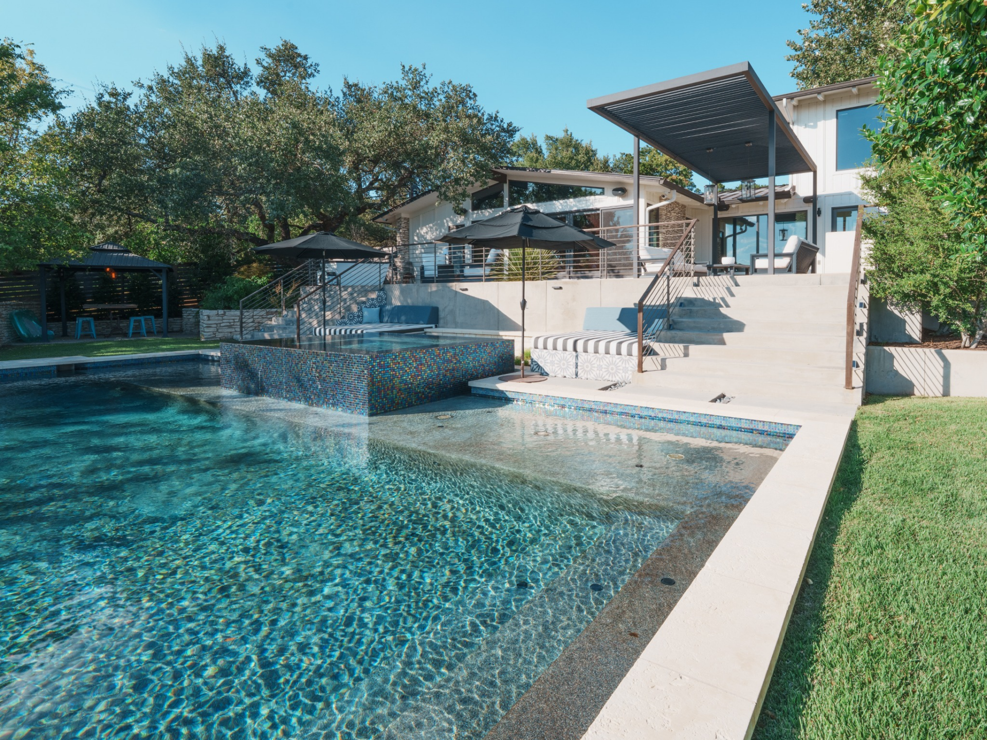 The pool terrace steps down from the upper deck, where a raised spa lined in mosaic tile spills into the main swimming area. 