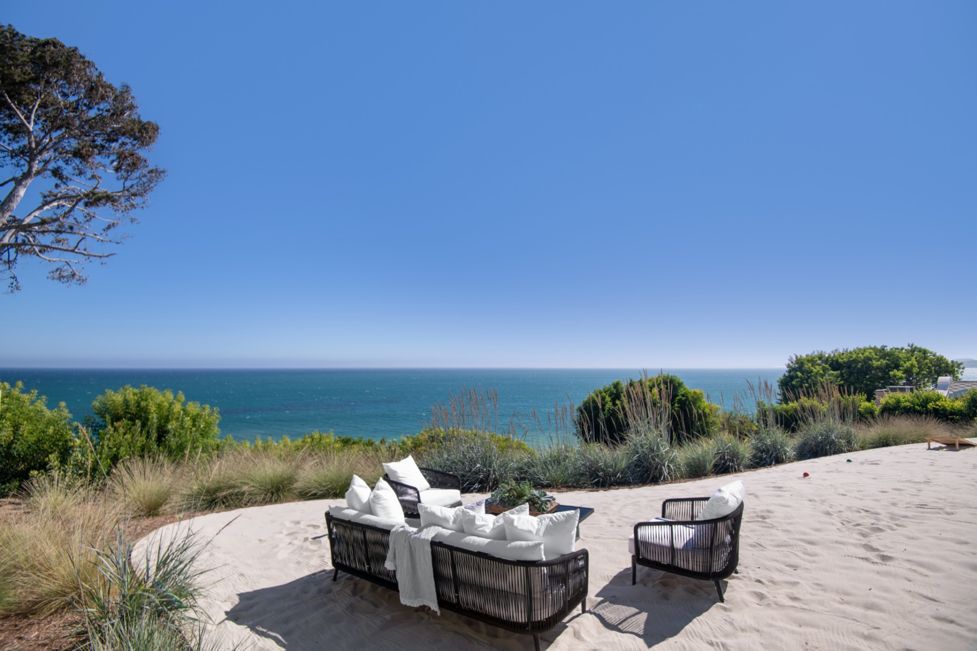 Surrounded by low grasses and planting beds, it is laid out more like a casual beach lounge, with seating grouped around a central table and open views straight out to the water.