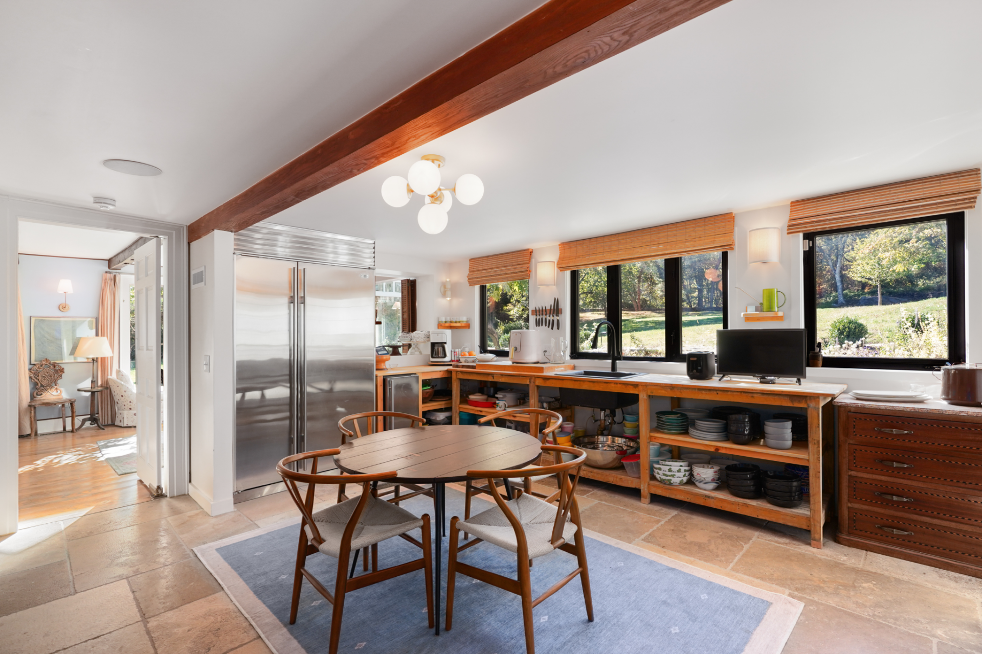Around the corner, the kitchen features a small round breakfast table that sits at the center and long counters that run beneath a row of black-framed windows.
