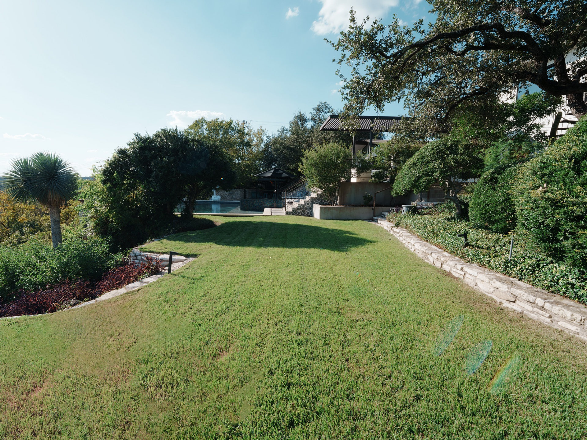 Beyond the terraces, a large lawn stretches outward, bordered by stone retaining walls and layered greenery.