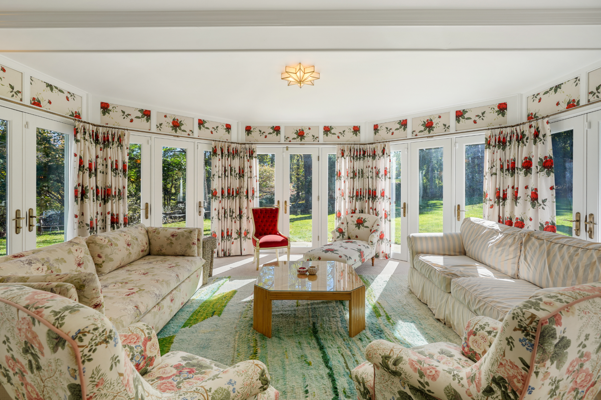The room is wrapped in windows and French doors on multiple sides, keeping it bright and tied to the lawn, while the lower ceiling makes it more casual than the great room.