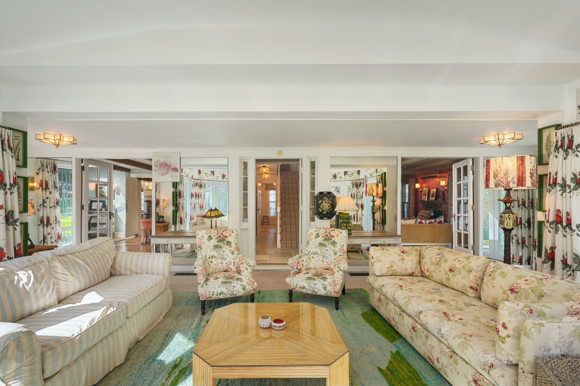 Floral upholstery, striped seating, matching drapery, and a large green-toned rug give the room a more layered look, while the layout centers on a low table surrounded by sofas and armchairs.