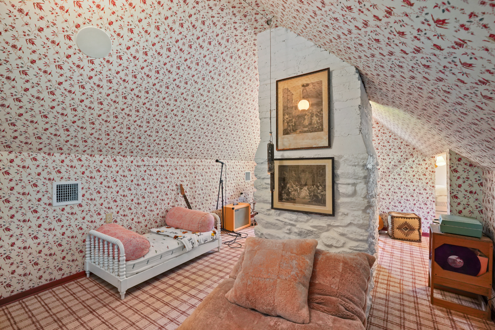 Set beneath a sloped ceiling, another bedroom leans fully into pattern, with matching floral wallpaper covering both the walls and ceiling. 