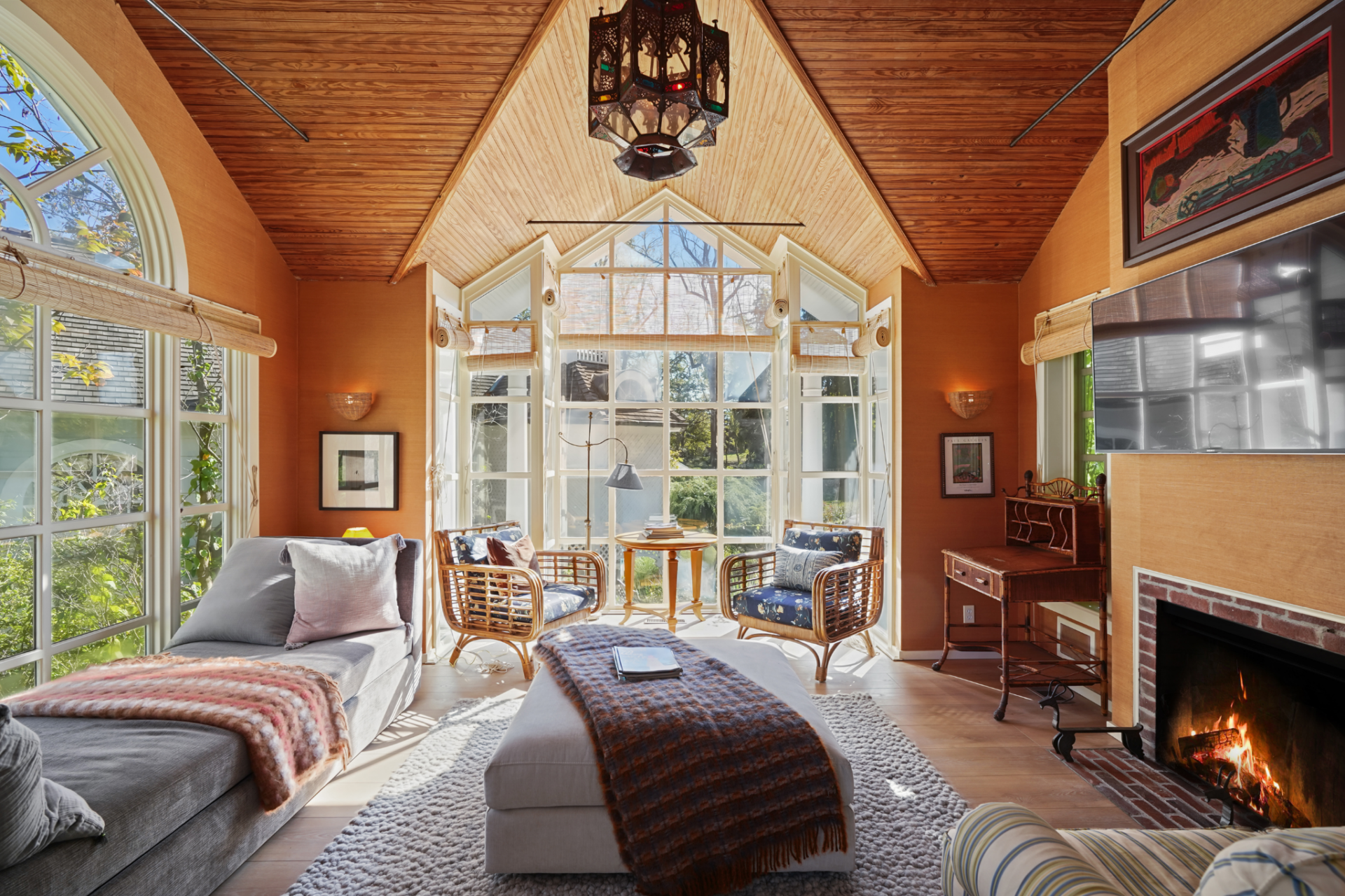 The living room sits beneath a vaulted wood ceiling with a minimal fireplace, tall windows, and a faceted bay at the far end.