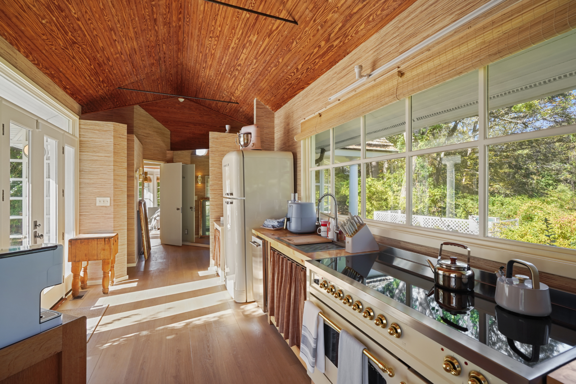 A cream-colored range and matching retro-style refrigerator give the room a more distinct identity, while the wood ceiling continues through the space and ties it back to the rest of the pool house.