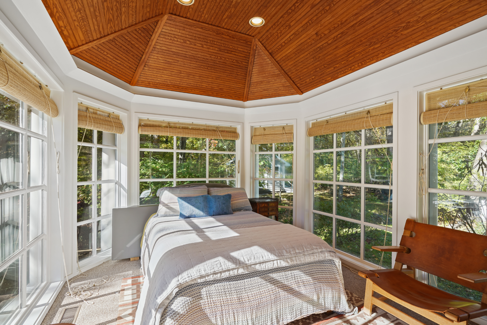  A bed sits at the center beneath a wood-paneled ceiling, with the surrounding glass making the landscape the room’s main backdrop.