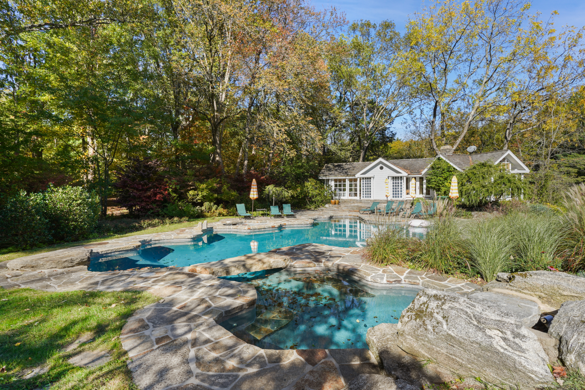 A raised spa sits in the foreground, while lounge chairs and planted borders wrap the perimeter and connect the water back to the pool house.