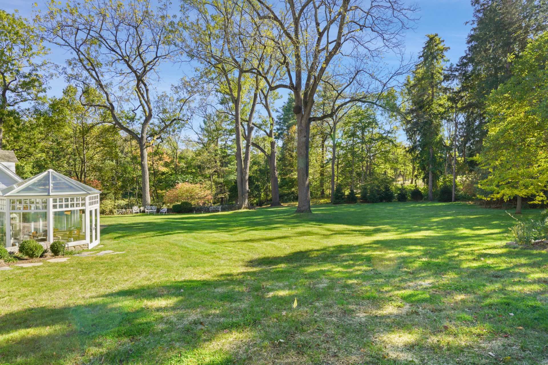 With small footbridges crossing through a reed-lined section of the grounds, the tree canopy thickens toward the edges, giving the property a mix of maintained lawn and gardens.
