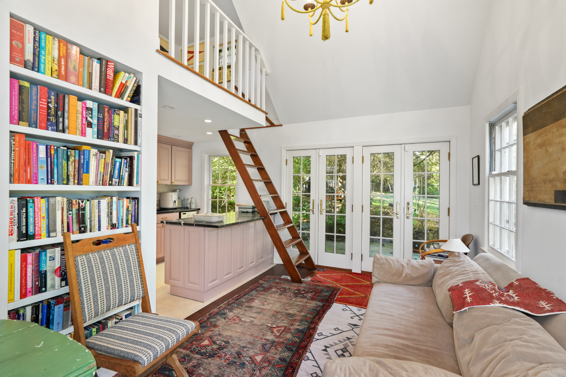 Built-in bookshelves line one wall, a sofa runs opposite, and French doors at the far end bring in light and connect the room directly to the surrounding greenery.