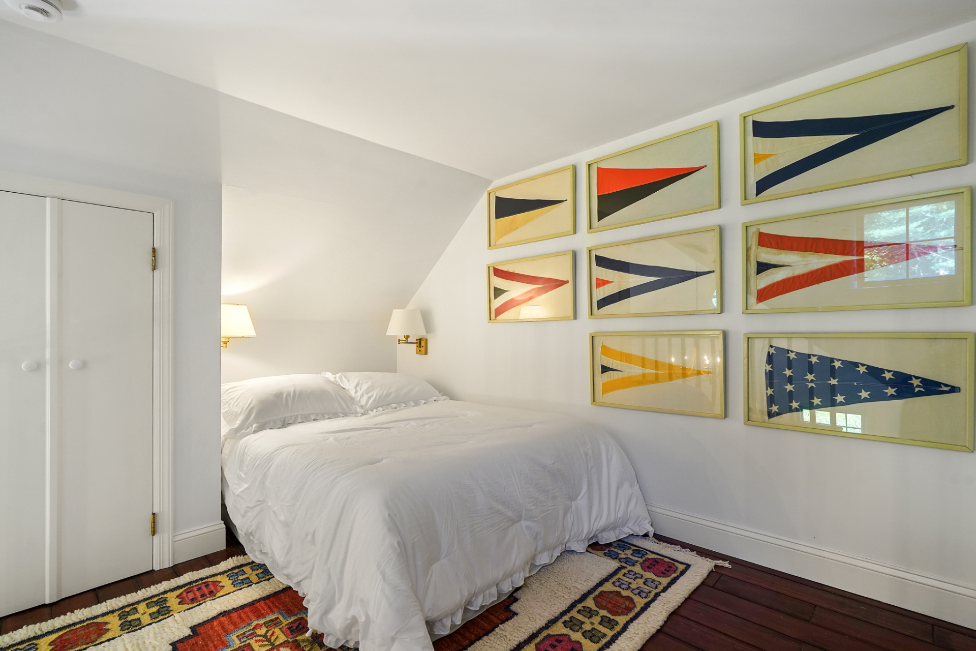 Up the ladder, the lofted bedroom is quite simple with dark wood floors, plain white bedding, and a grid of framed nautical flags.