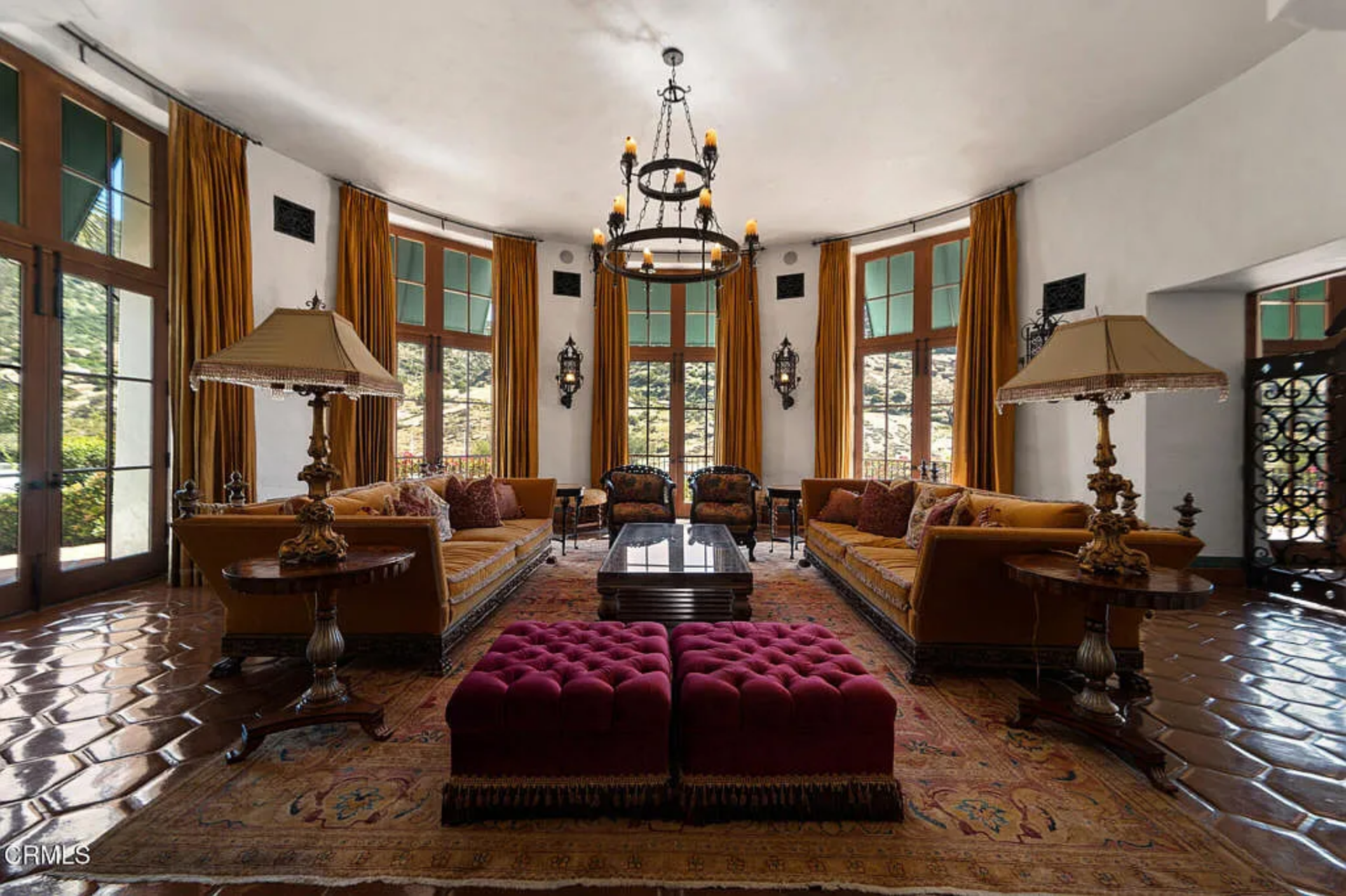 A ring chandelier hangs over the center, while two long sofas face one another across a dark coffee table and a pair of tufted ottomans, giving the room a clear, balanced layout from the moment you walk in.