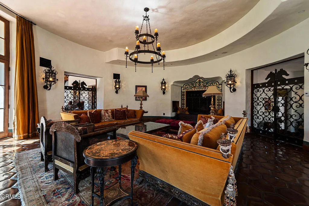 Rust-colored drapery, terracotta tile floors, carved wood tables, and iron detailing give the space a more traditional Mediterranean character, with the seating grouped tightly enough to keep the large room from feeling too spread out.
