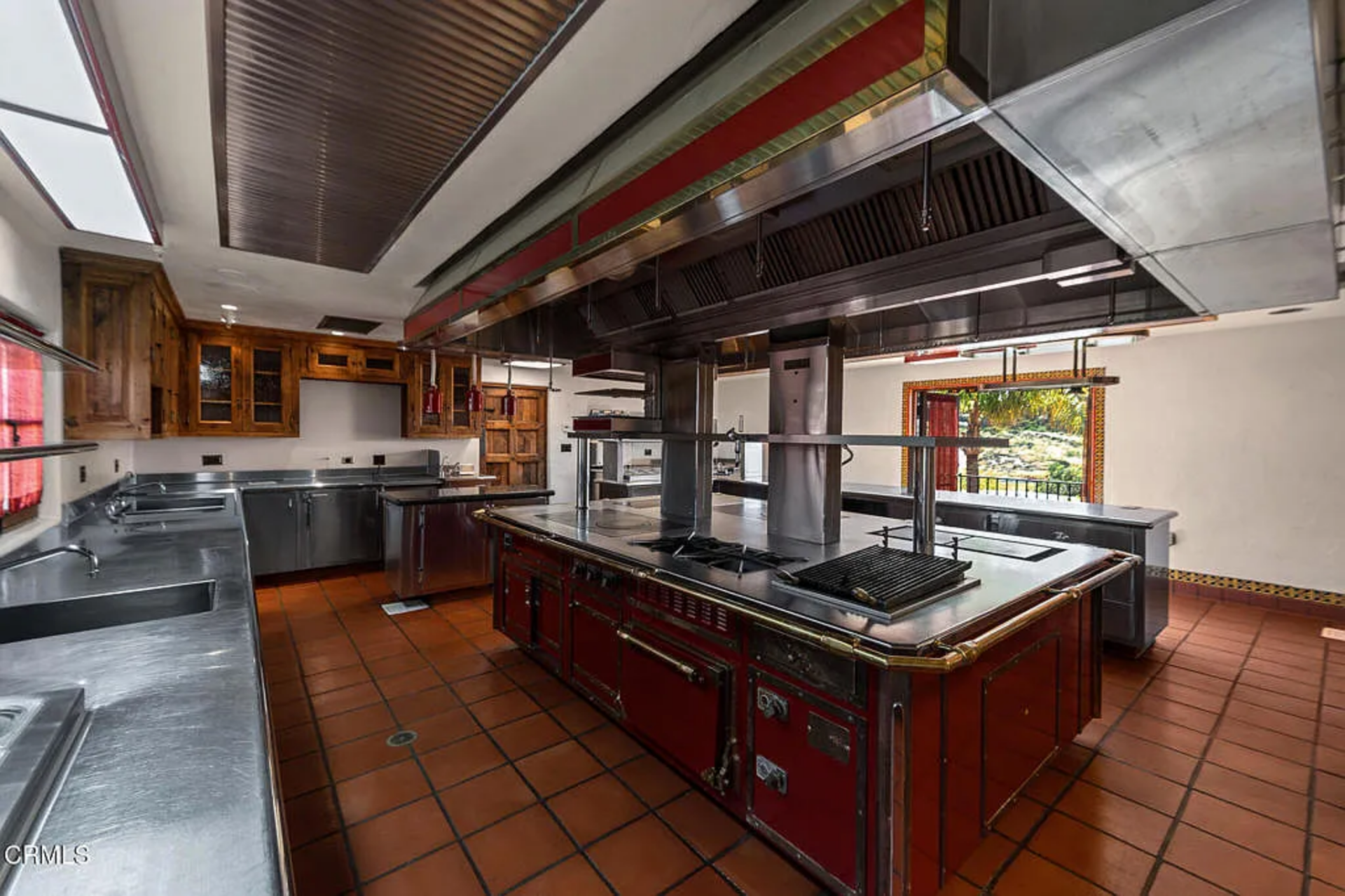 Red base cabinetry and terracotta floor tile tie it back to the villa’s overall palette, while long perimeter counters, deep sinks, warming and service stations suggest it's been designed to support large events.