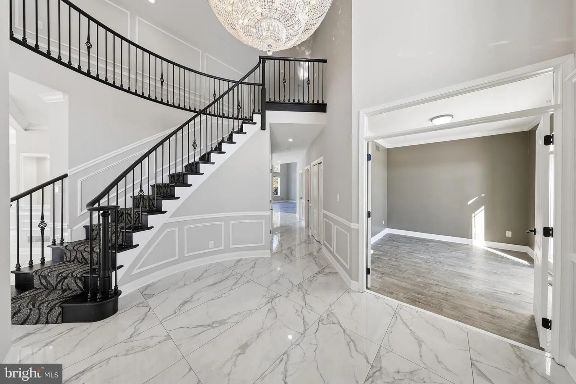 The sweeping curved staircase, lined in dark wood treads and black wrought-iron balusters, rises to a second-floor overlook, creating a grand focal point that sets the tone for the rest of the estate.