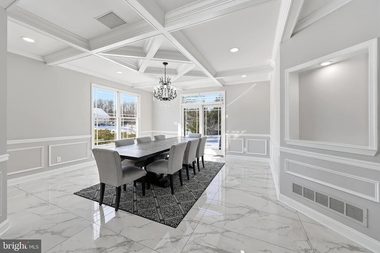 Overhead, a coffered ceiling adds architectural depth, anchored by a regal chandelier that centers the room around a long dining table for eight. 