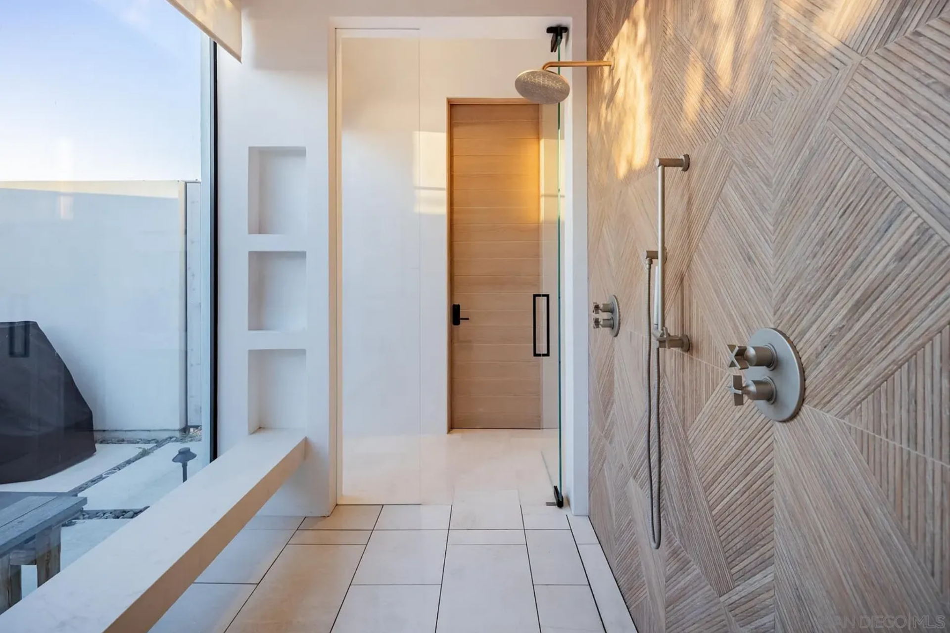 The walk-in shower is enclosed by a patterned feature wall, which holds the fixtures, including an oversized rain head, while the other side is lined with a full wall of glass looking out to the courtyard.
