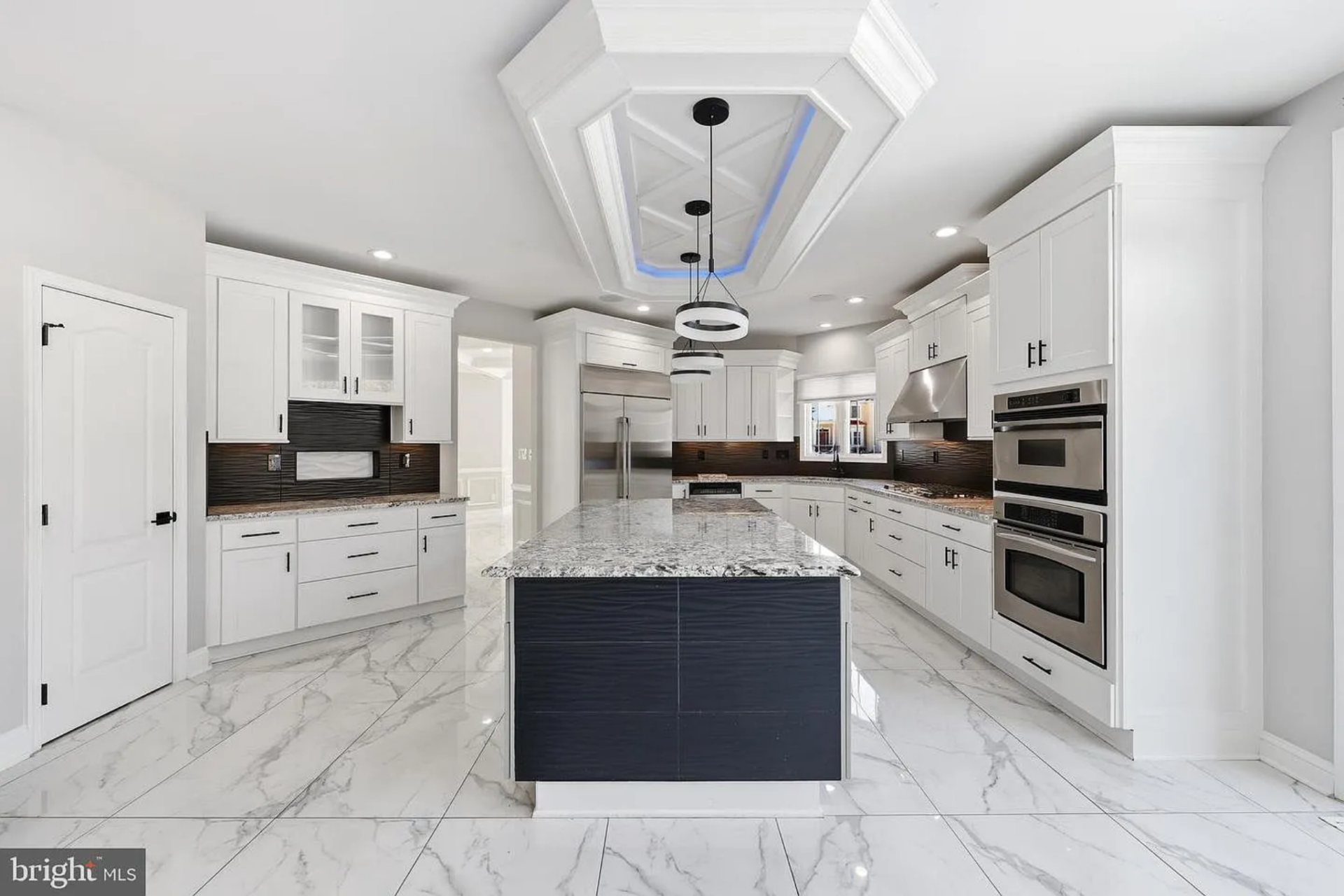 Around the corner, the updated gourmet kitchen features white shaker-style cabinetry that wraps the perimeter, contrasted by a dark, textured backsplash that adds depth behind the counters and cooking areas.