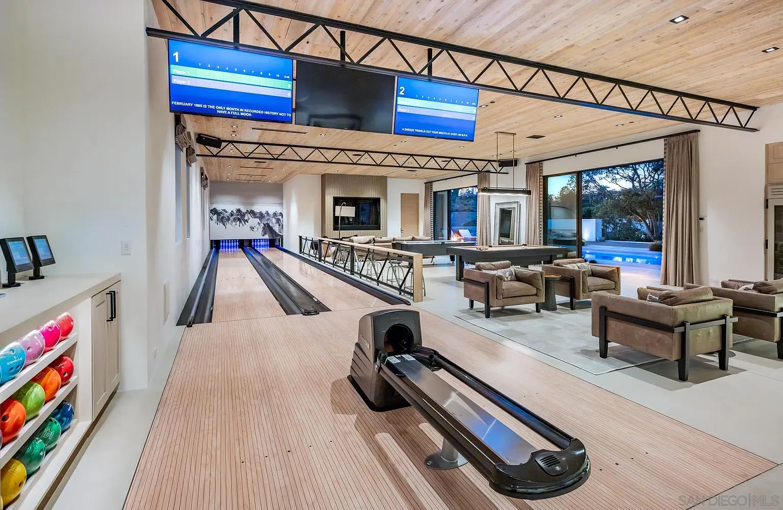A two-lane bowling alley runs along one side, while the center of the room is lined with a pool table, an air hockey table, and a media area at the far end.