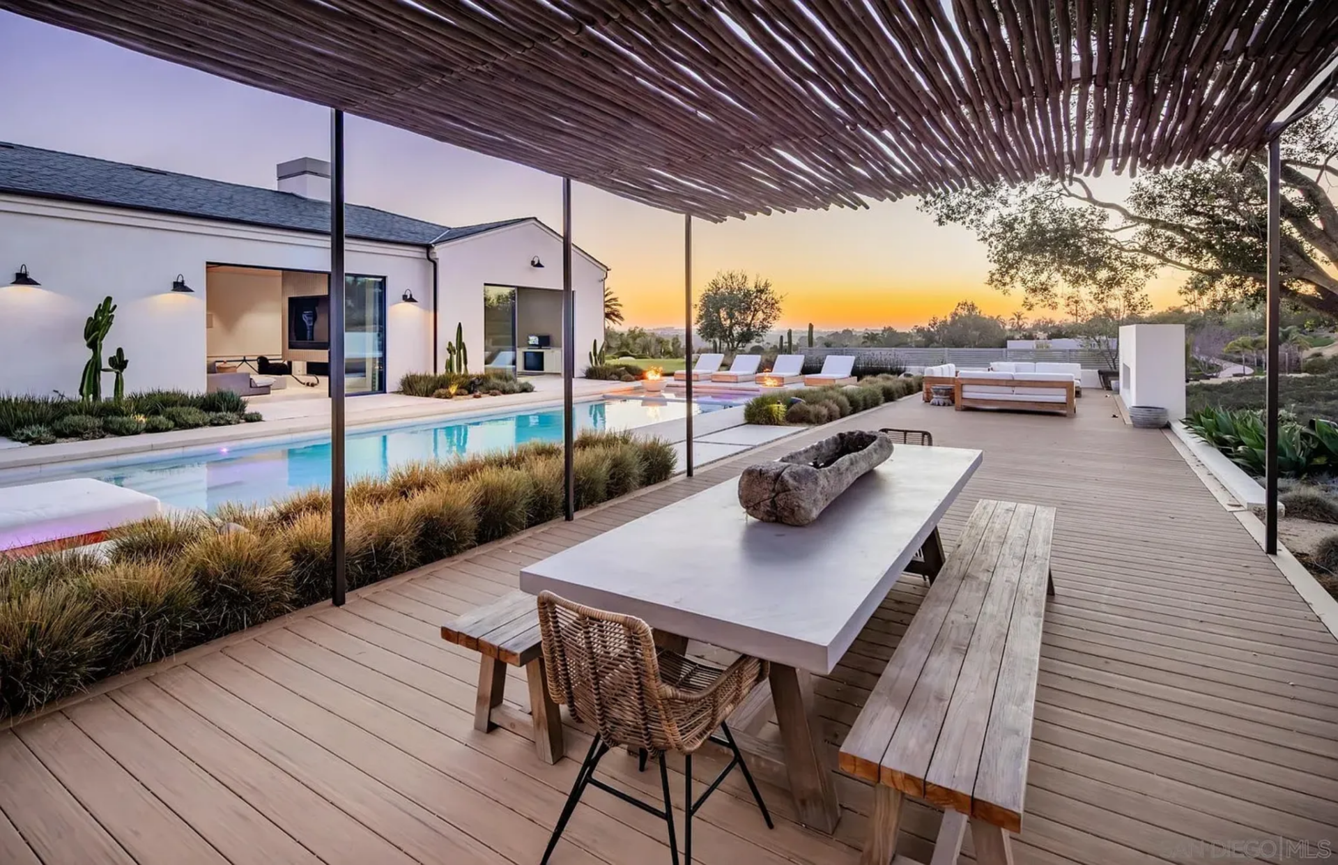 A little farther out, the dining area sits beneath a slatted pergola that filters the light and frames long views back across the pool and house. 