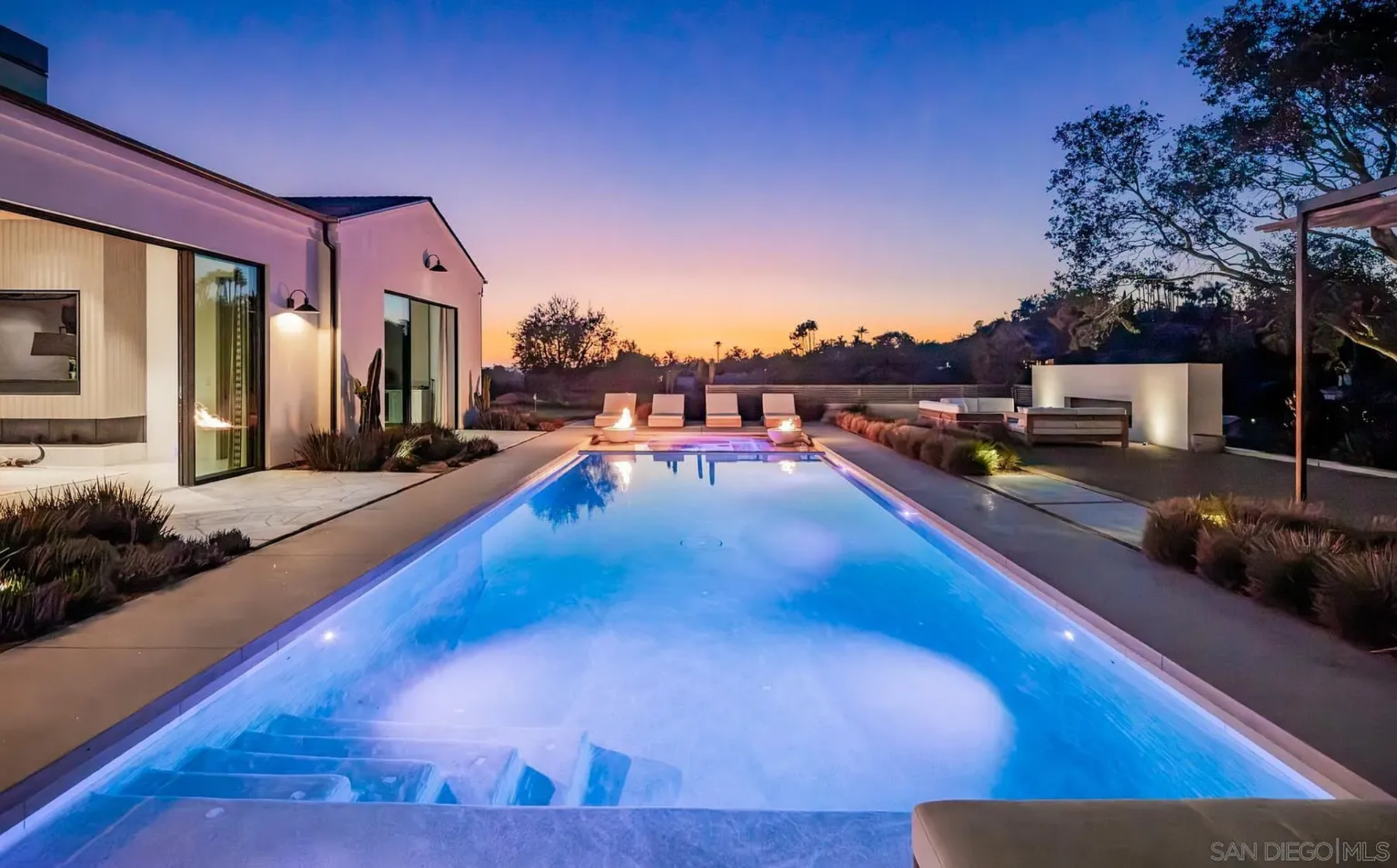  At dusk, the water becomes a focal point, with the illuminated pool, inset spa, and fire features at the far end creating a strong visual line that pulls the eye straight through the outdoor spaces.