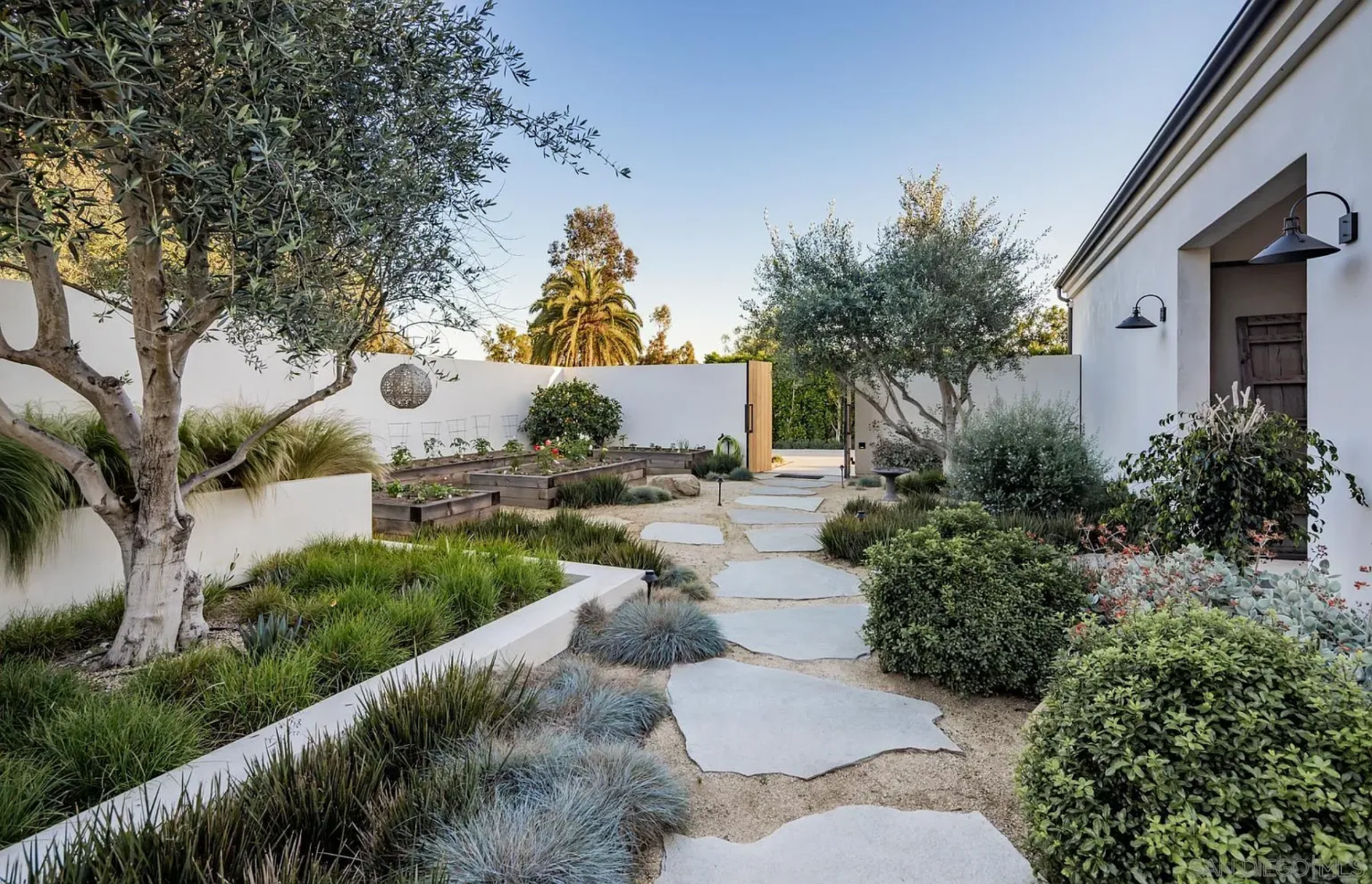 Lastly, along a gravel path, the garden adds a quieter outdoor space with raised plant beds and layered greenery that soften the sharper edges of the home.