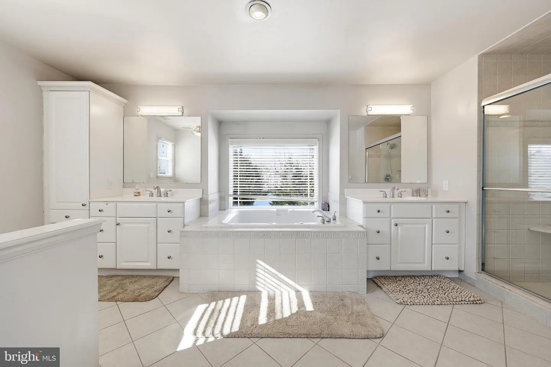 The en-suite bath is arranged symmetrically, centered around a large soaking tub set beneath a wide window. 