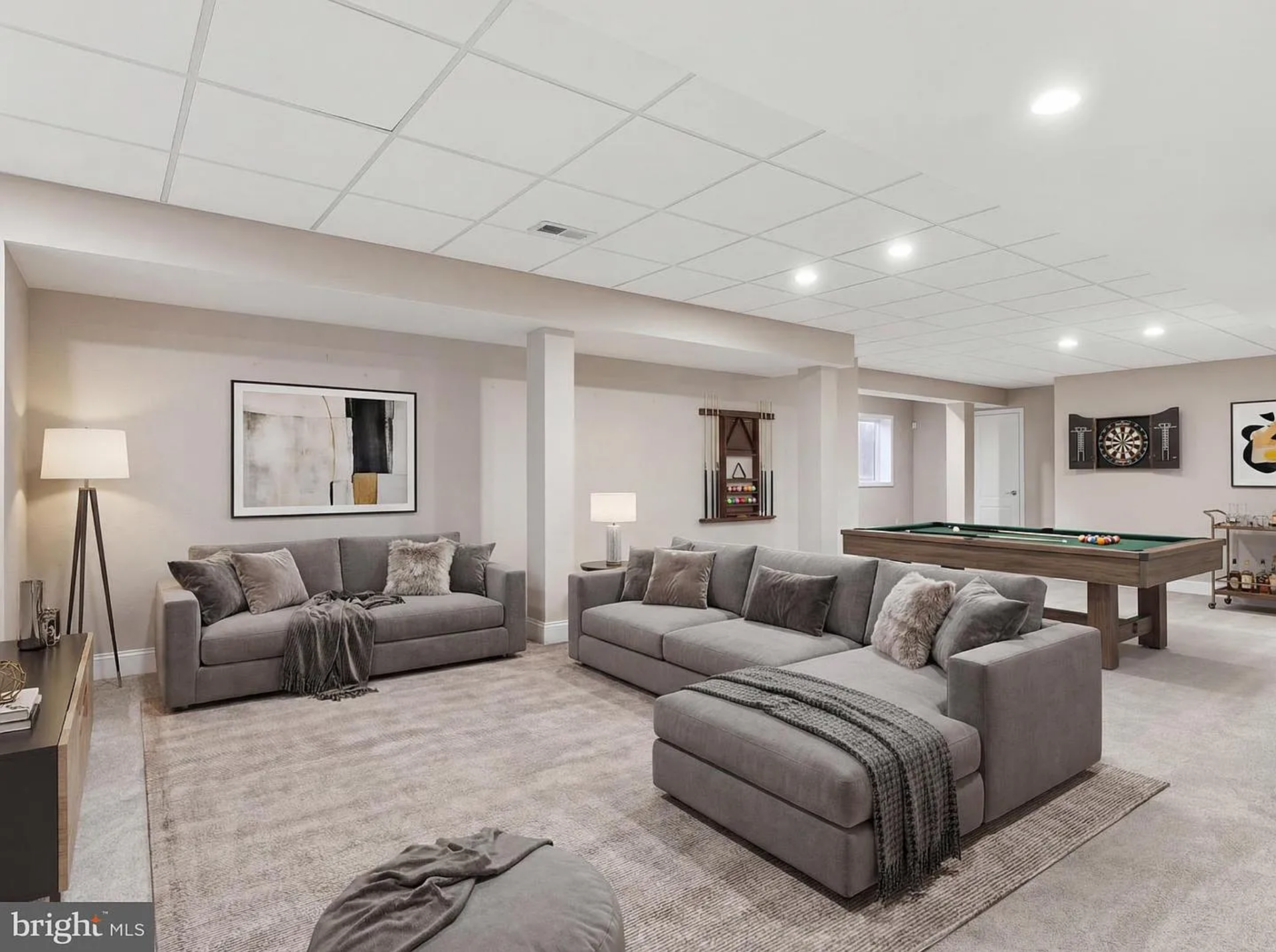 The main recreation area has a large open seating layout, with plush carpeting underfoot and neutral walls that keep the space bright despite being below grade. 