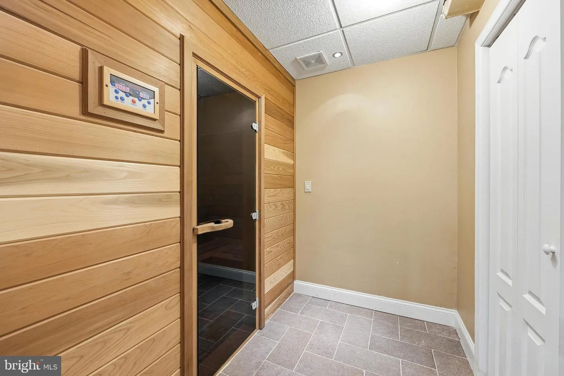 The wood-paneled interior and glass door entry give the sauna a dedicated spa-like look, while the tiled flooring outside ensures durability and easy maintenance.