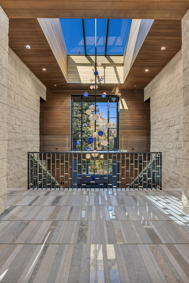 A unique hanging sculpture with vibrant blue and copper-colored spheres cascades from the high ceiling, adding an artistic and modern touch between the skylight and the sleek staircase.