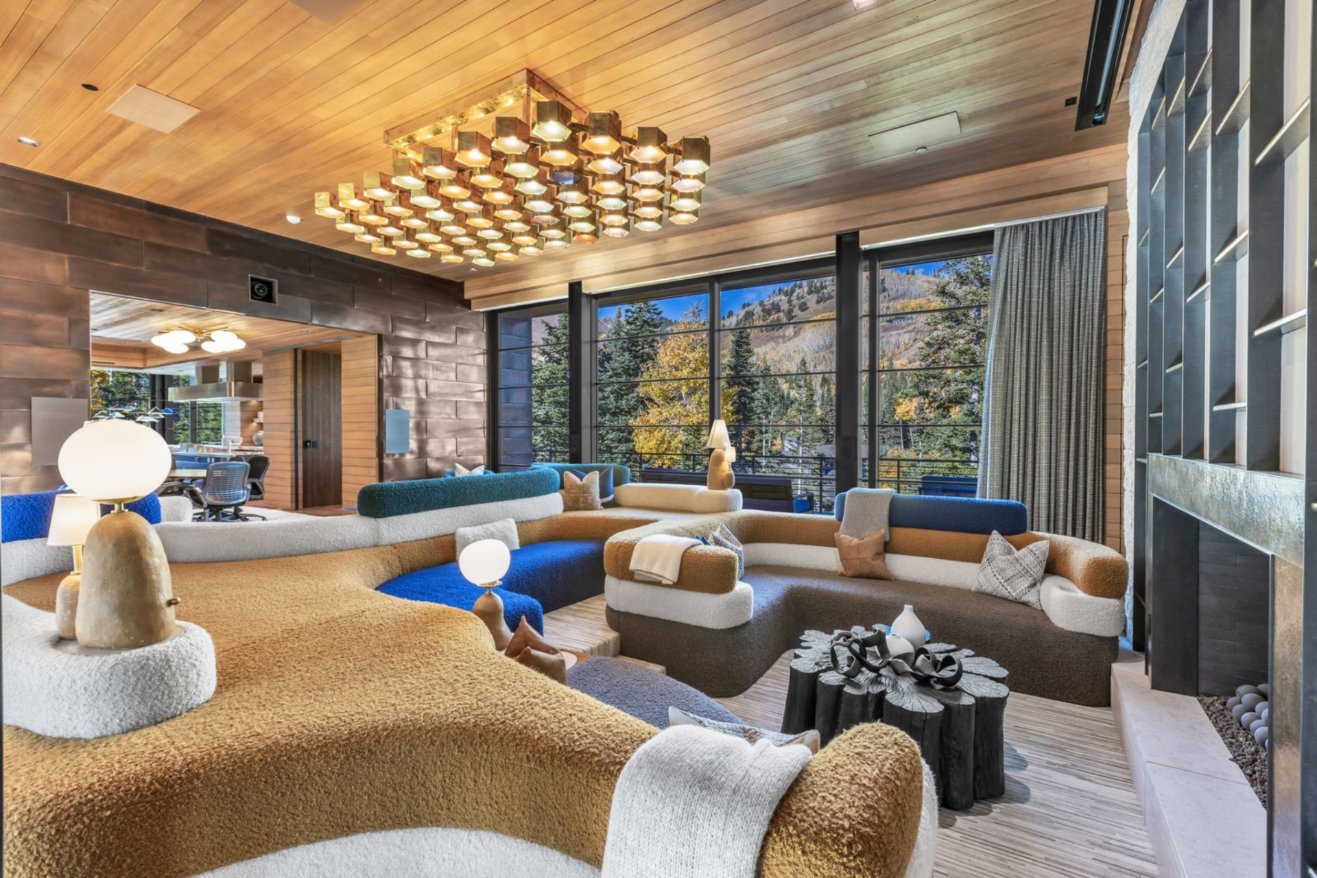 The seating arrangement is built around multiple curved sectionals that wrap around the room, upholstered in layered tones of camel, cream, charcoal, and deep blue.