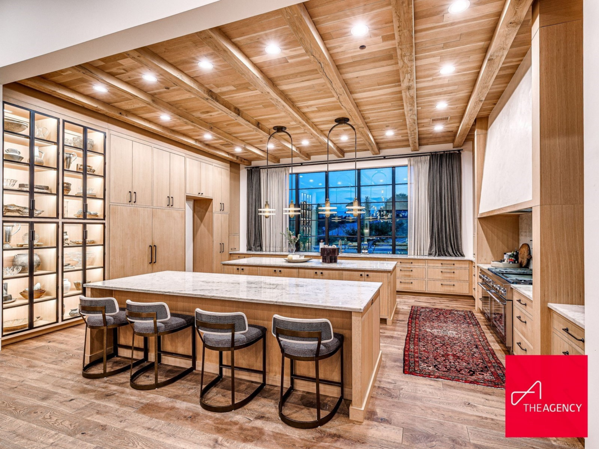 The room is built around double marble-topped islands, each finished in light wood cabinetry with black hardware that ties into the home’s modern detailing.