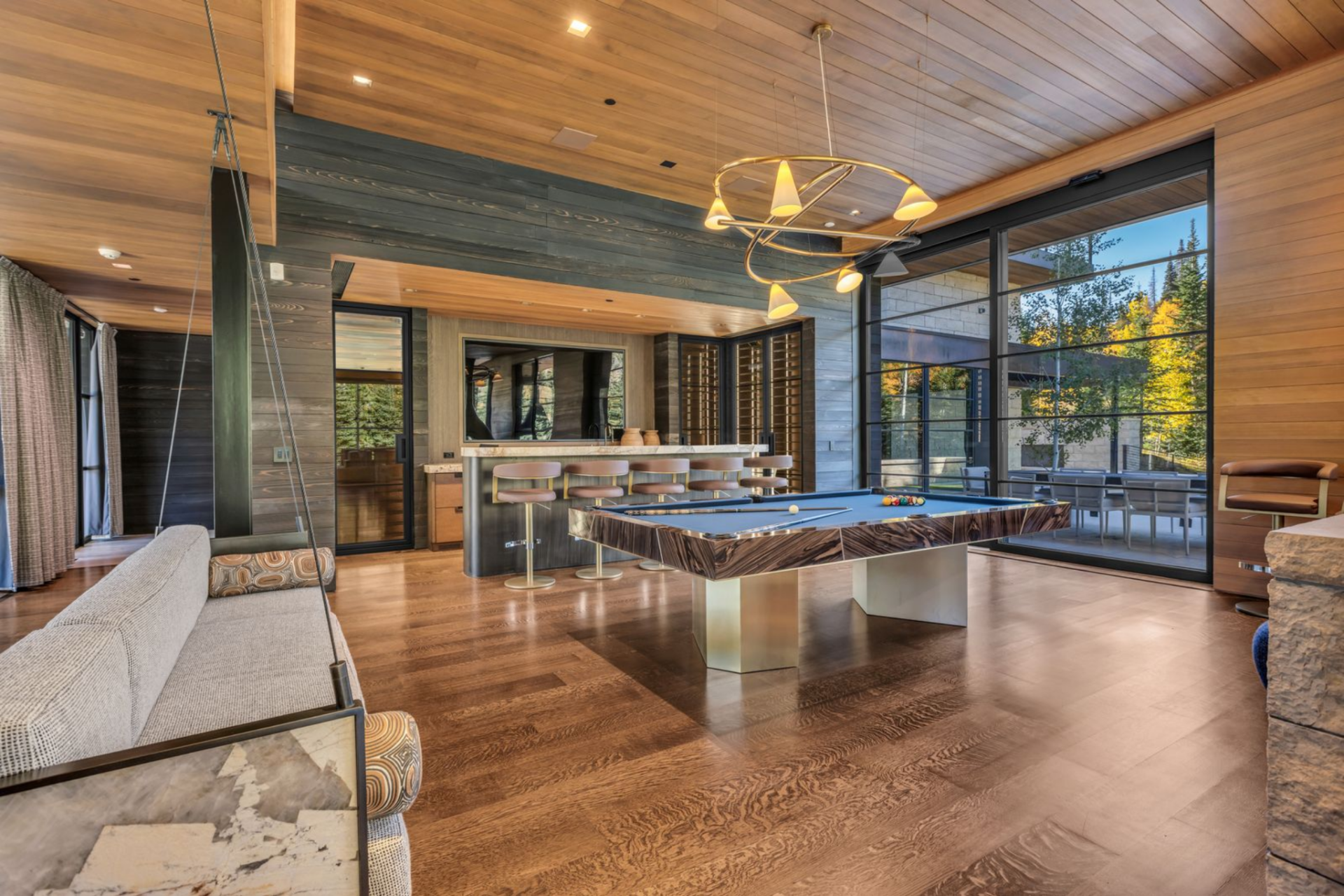 The room features a custom pool table with a richly grained wood surround and bold blue felt, set atop wide-plank hardwood floors.