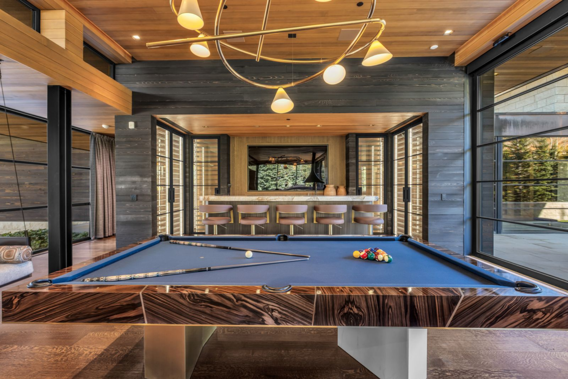 Along the back wall, a full bar is framed by darker horizontal wood paneling, creating contrast against the lighter tones throughout the rest of the home.
