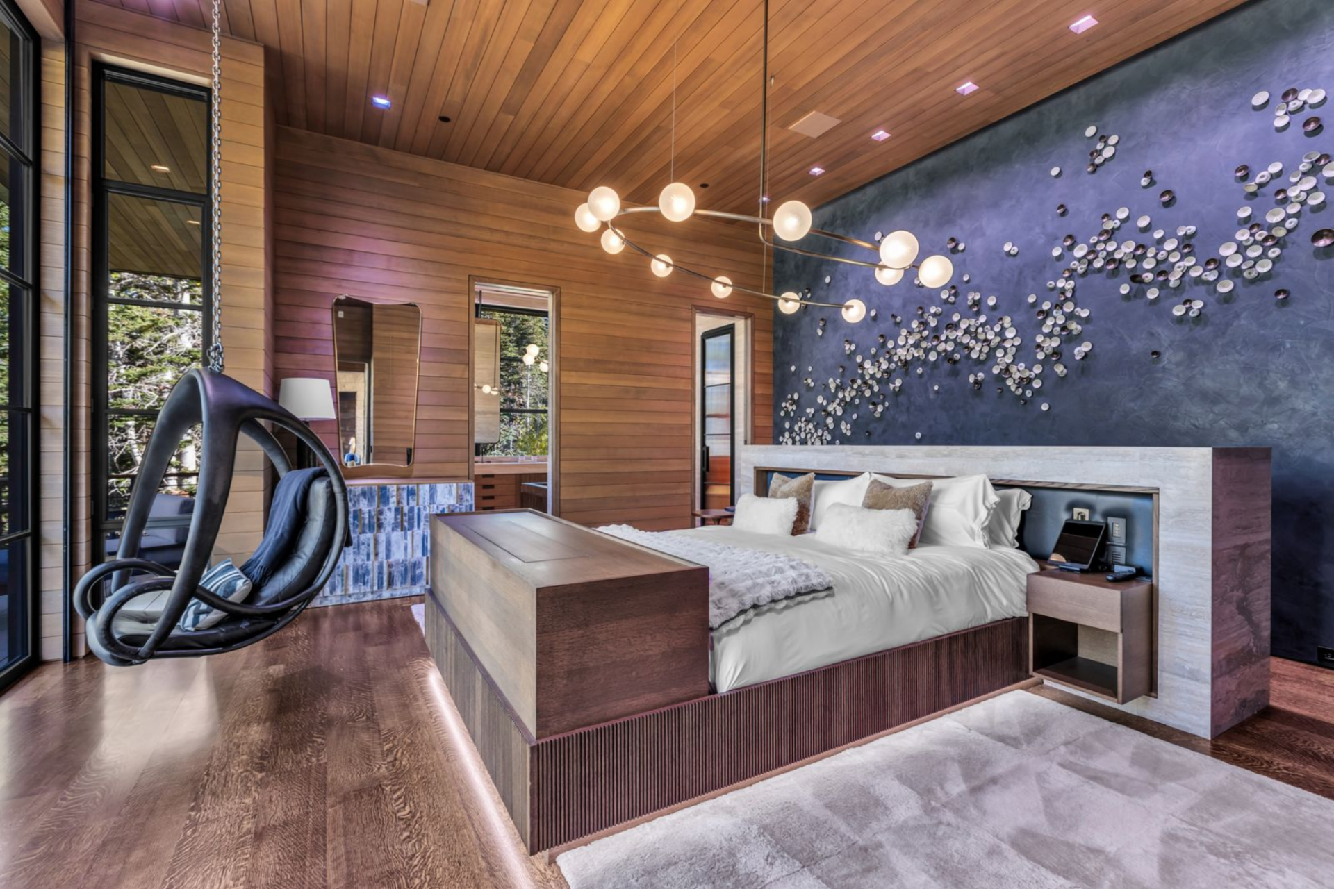 The sleeping area features a wood-framed bed set against a dramatic, deep-blue accent wall adorned with sculptural metallic artwork.