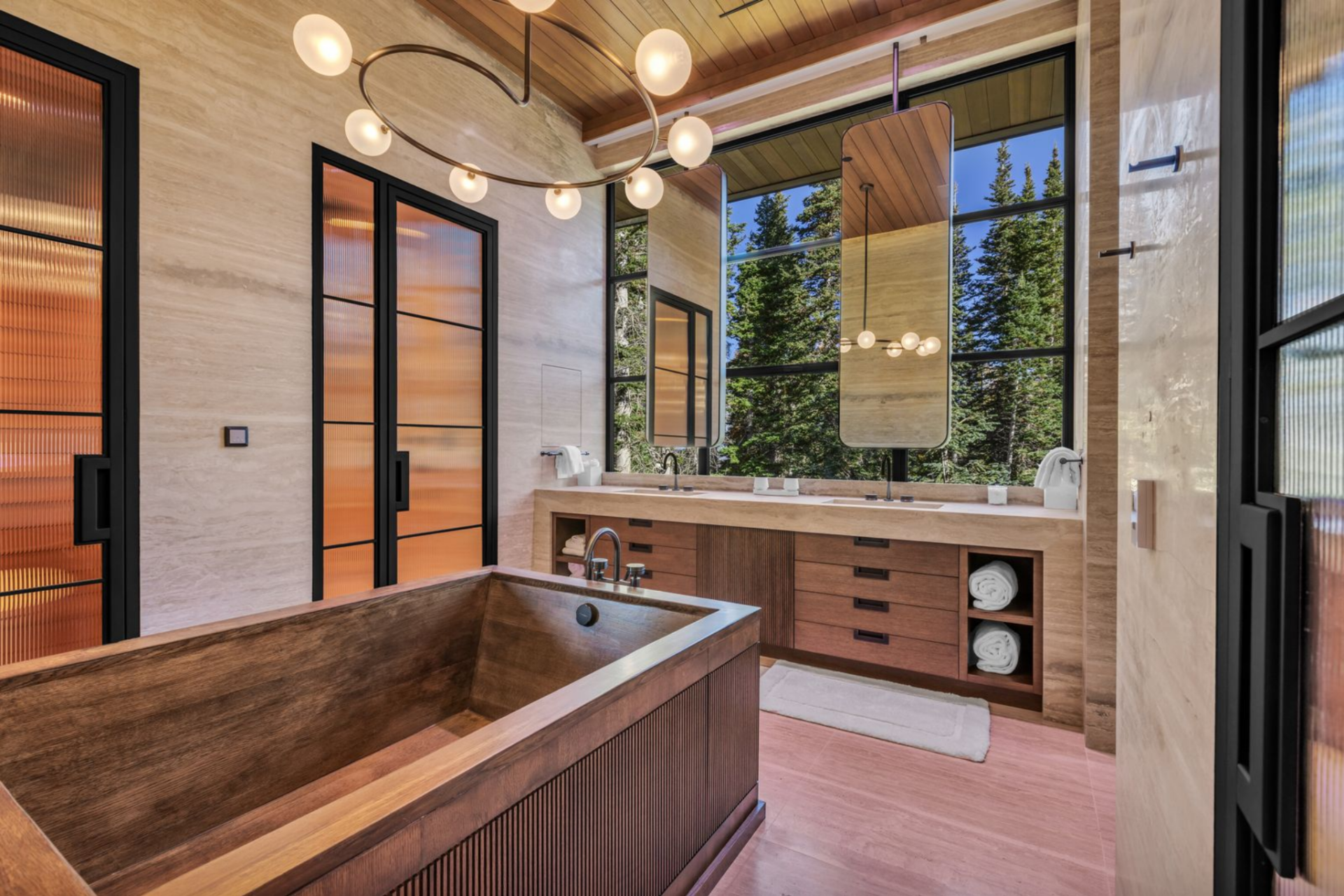 A freestanding, wood-wrapped soaking tub sits in the center of the space, positioned beneath statement lighting and next to a glass-enclosed shower.