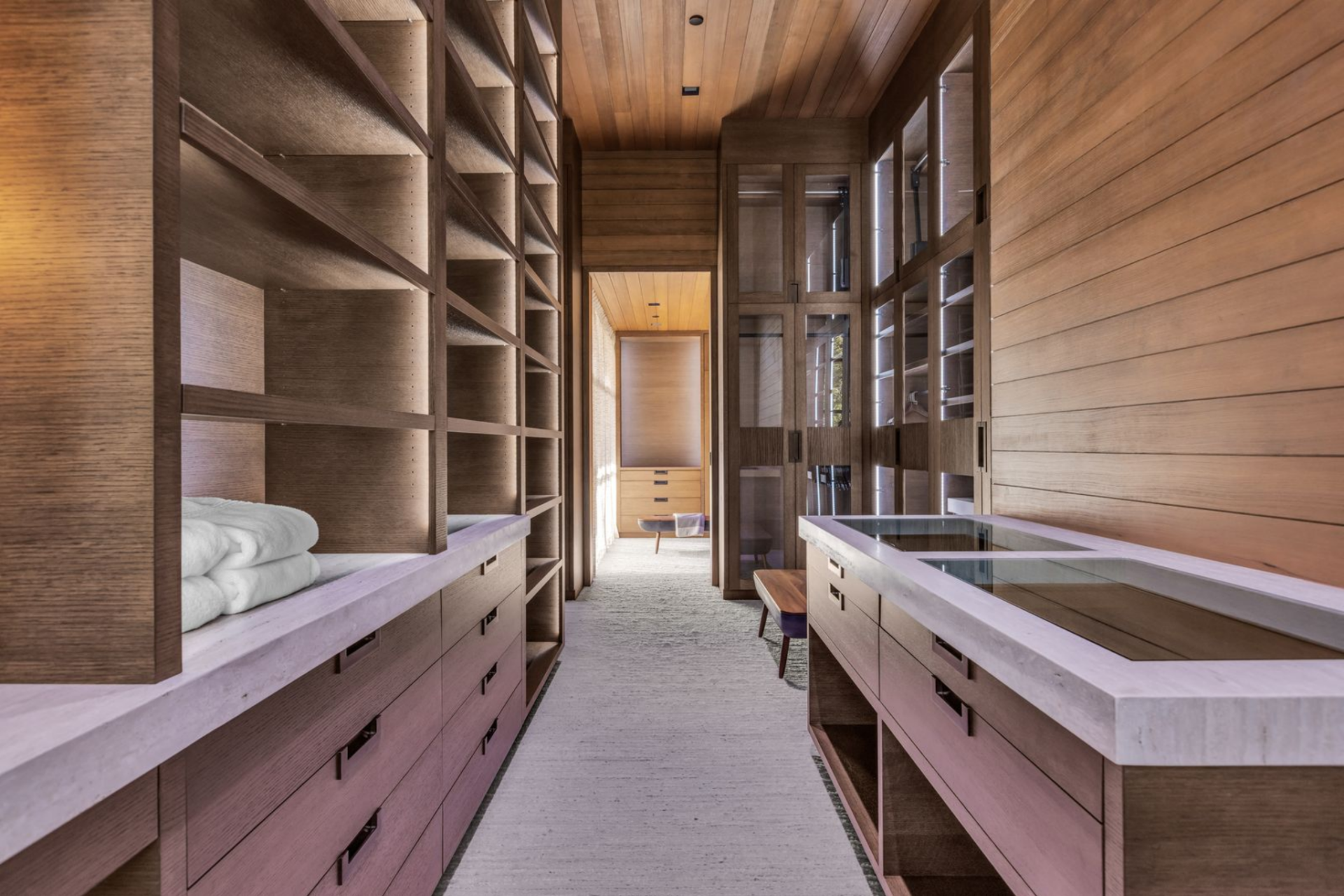 The walk-in closet is designed with full-height custom shelving, integrated lighting, and extensive drawer storage along both sides, creating a boutique-style dressing corridor.