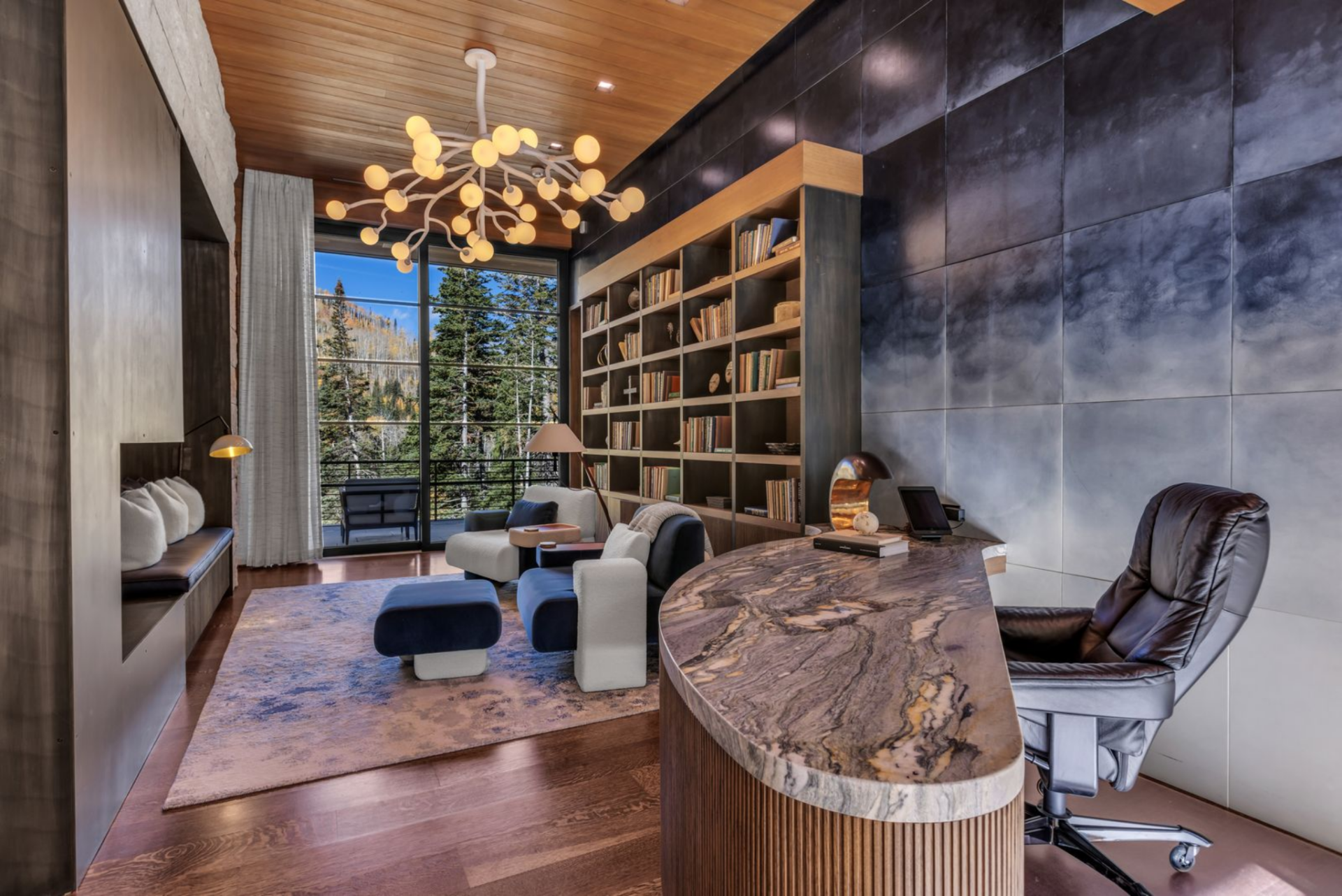 The executive office features a curved stone desk with dramatic veining, positioned to face a wall of built-in shelving filled with books and curated decor.