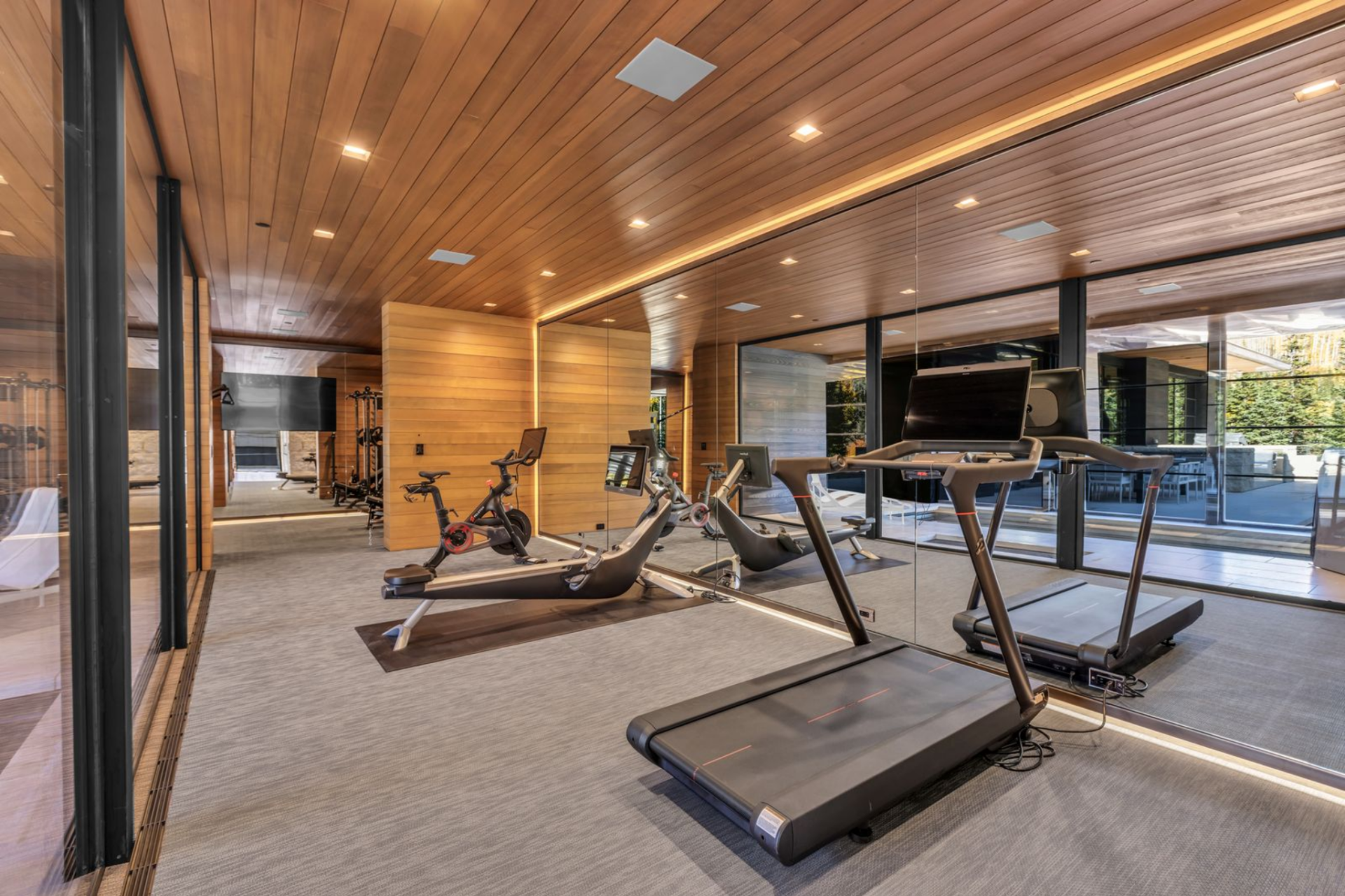 The private fitness studio features mirrored walls, wood-paneled ceilings, and professional-grade equipment, including treadmills and stationary bikes.