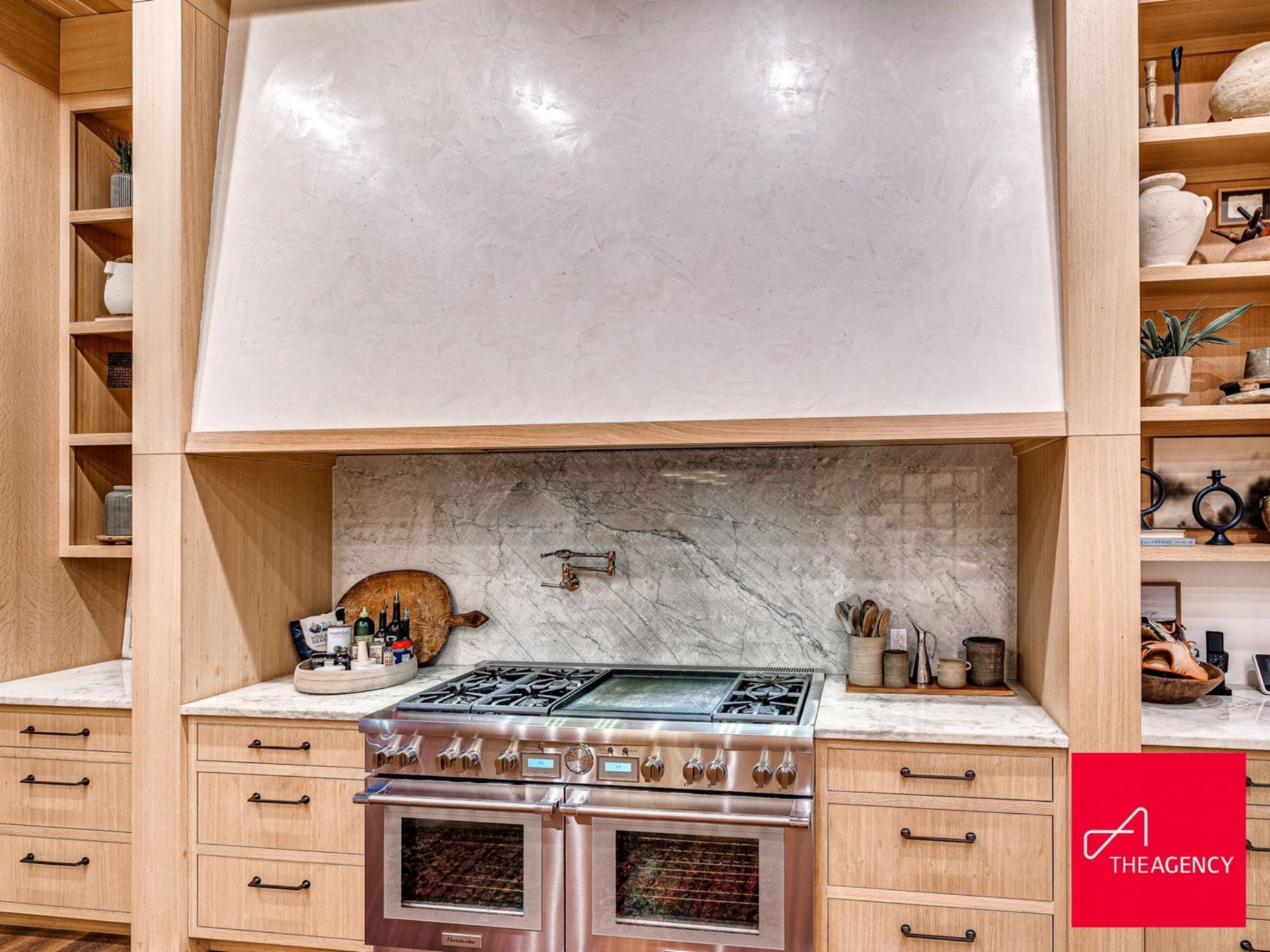 Along the perimeter, premium stainless steel appliances are built directly into custom cabinetry, including a professional-grade range set against a full-height stone backsplash.
