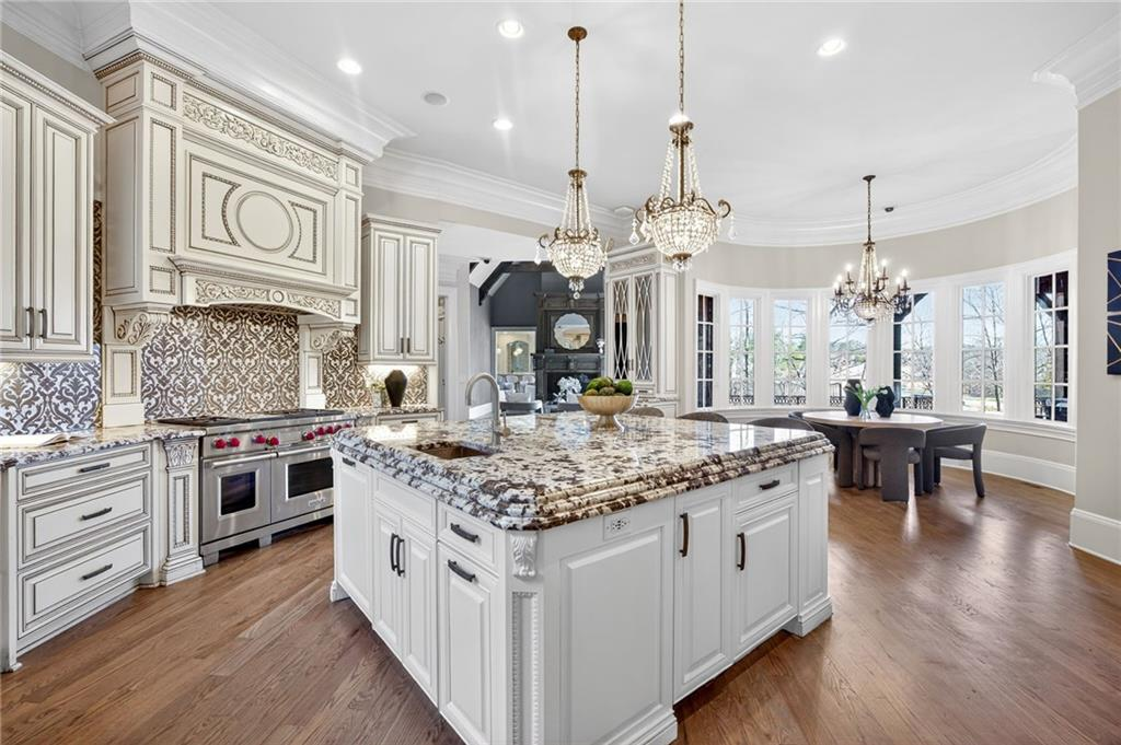 Custom white cabinetry with intricate detailing surrounds the room, complemented by patterned tile backsplashes and a professional-grade range with premium Sub-Zero and Wolf appliances.