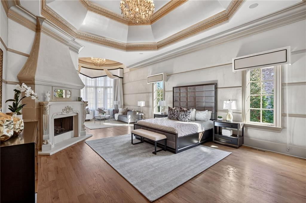 The bedroom centers around a large sleeping area framed by a fireplace and an adjacent sitting space set within a bright window alcove. 