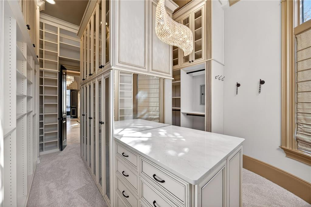 The suite is completed by a striking two-story custom closet lined with built-in shelving, glass-front cabinetry, and extensive drawer storage.