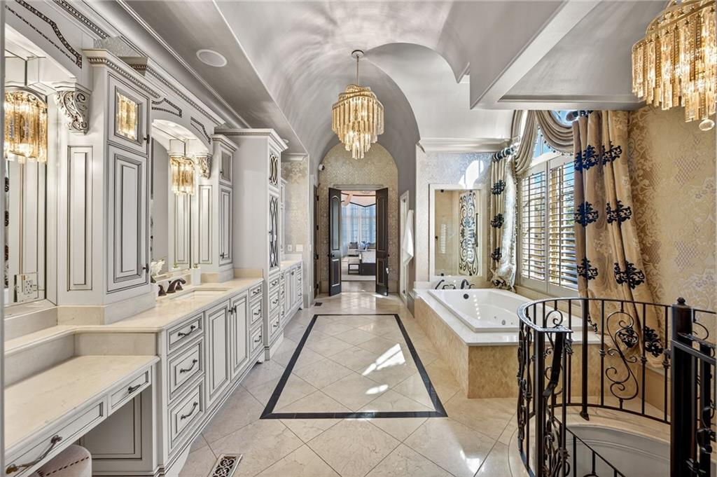 The spa-style bathroom extends the suite with an expansive layout that includes dual vanities, detailed cabinetry, and a soaking tub positioned beneath large windows.
